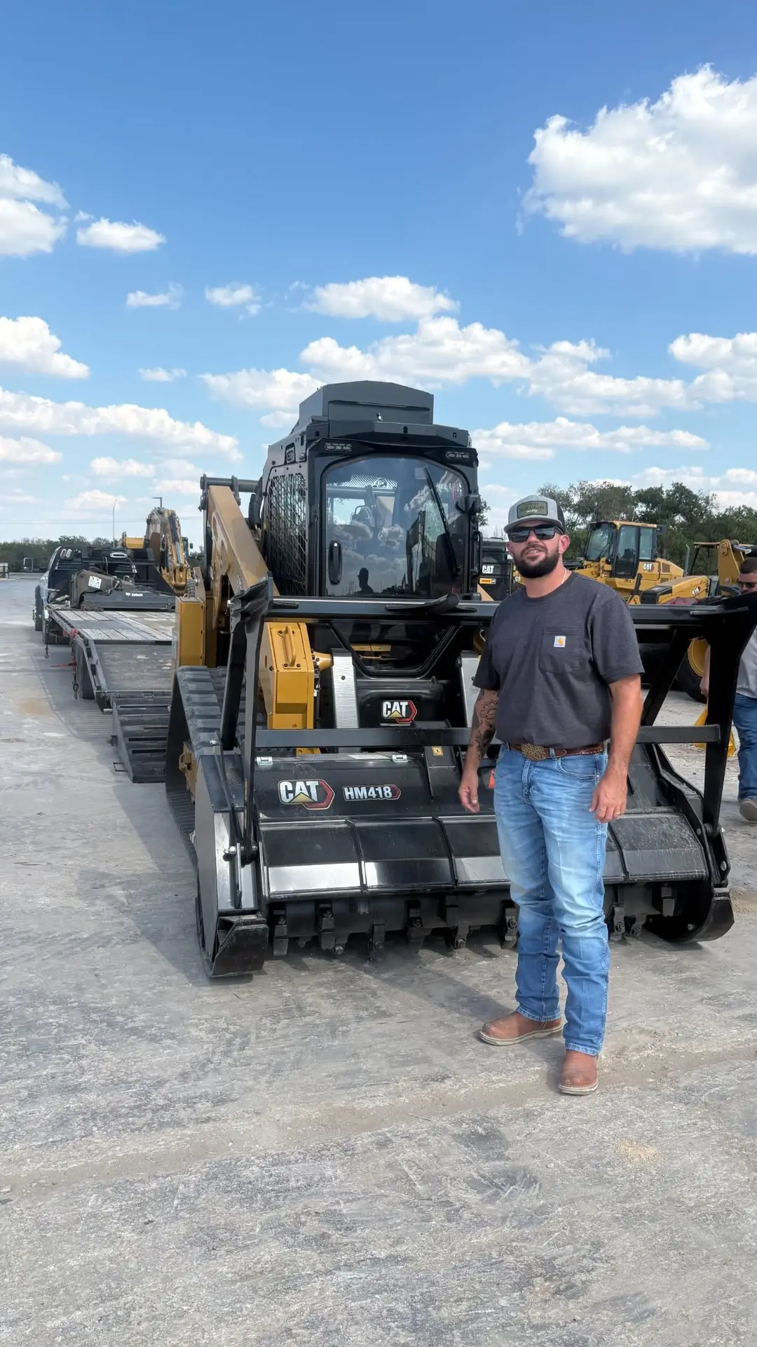 Hilliland Contracting operator standing next to a CAT compact track loader with HM418 forestry mulching head on a flatbed trailer in Seguin, TX