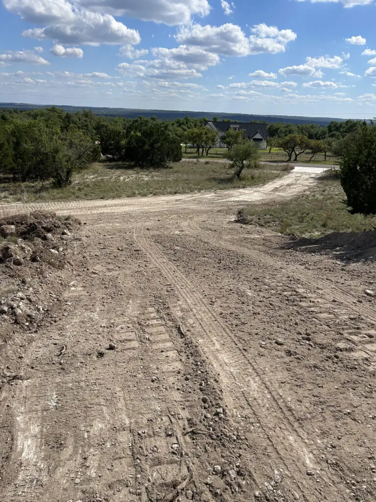 Hilliland Contracting grading a rural driveway on a Texas Hill Country property with a ranch home visible in the background near Seguin, TX